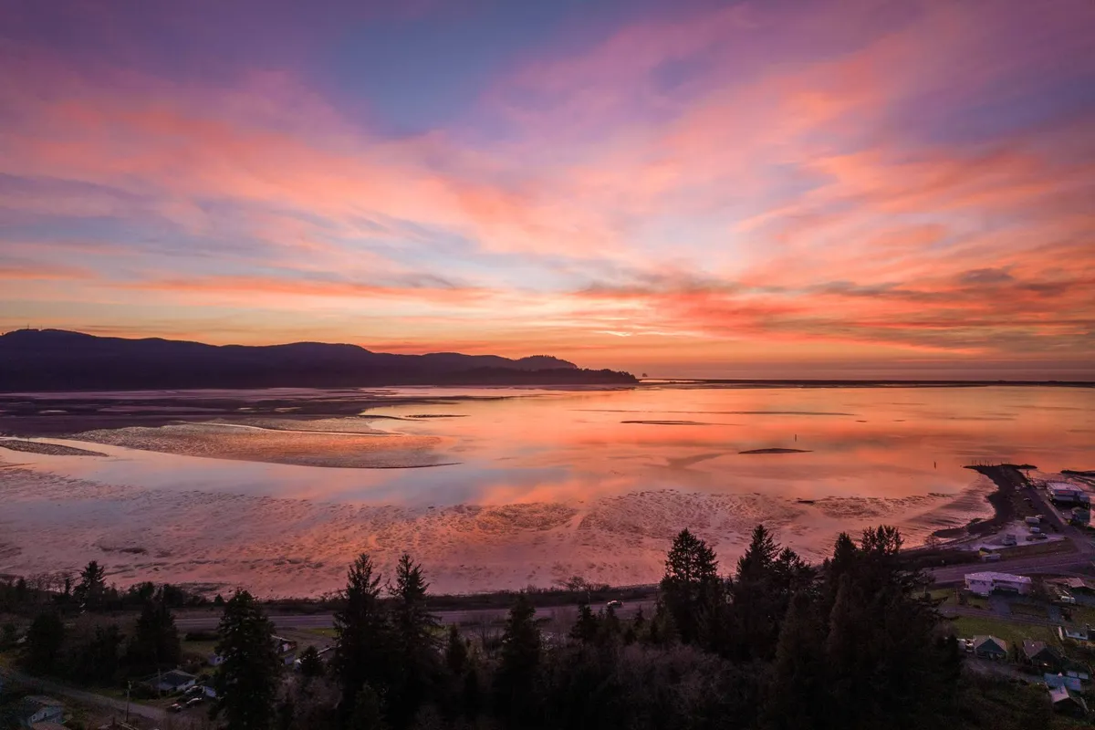 A stunning view of the sun setting over the water, with a mountain silhouette and reflective surface. The tranquil mood emphasizes the natural beauty and serenity of the bay, inviting quiet contemplation or evening wine on the deck.