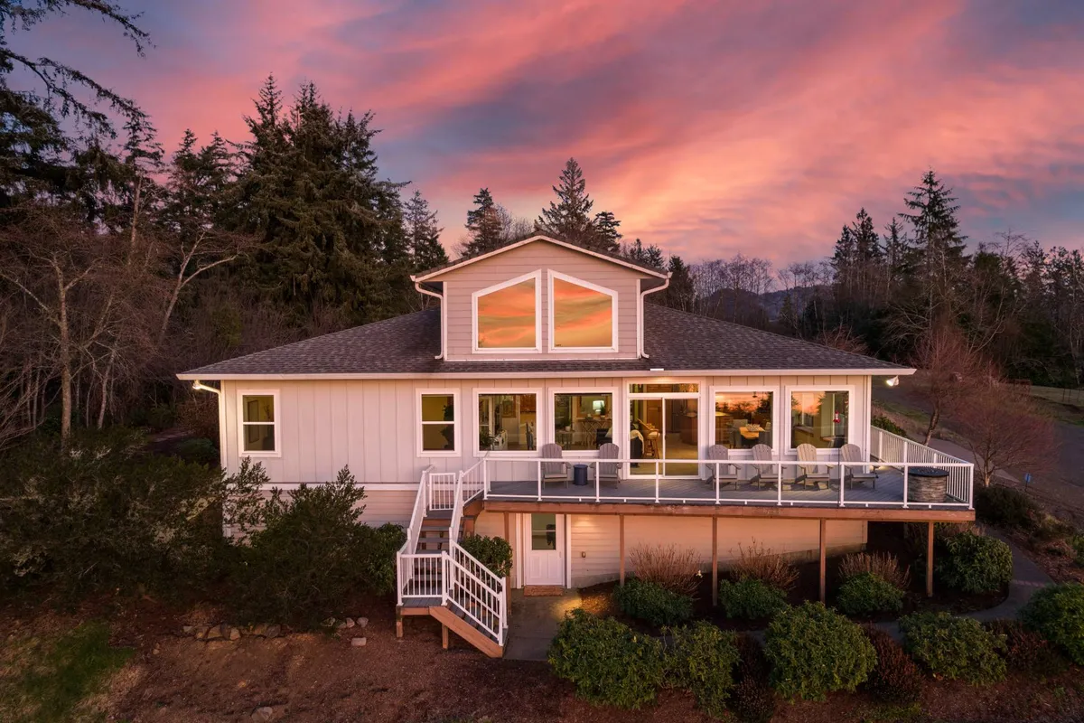 This image captures the exterior of Bay View Villa highlighted by its spacious deck, set against a glowing sunset sky. The deck provides ample space for social gatherings and showcases panoramic views, with the house and its inviting atmosphere clearly visible.
