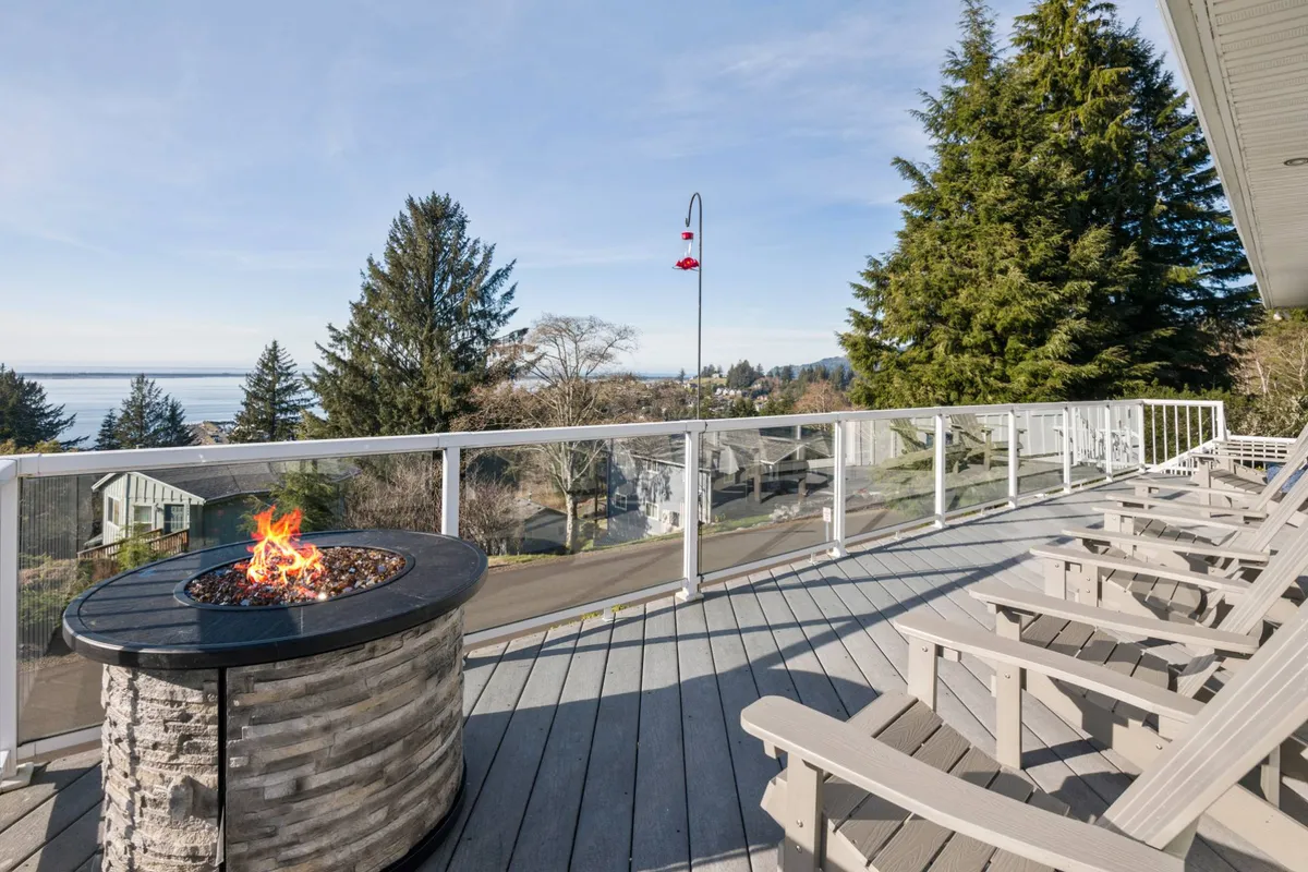 A welcoming deck area featuring a fire pit surrounded by comfortable deck chairs, with a serene view of the water and trees in the background. The scene is set for social gatherings or peaceful evenings by the fire.