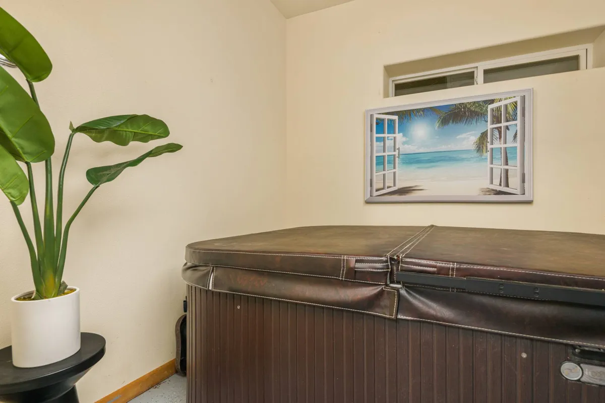 A tranquil indoor setting featuring a hot tub surrounded by potted plants and a framed beach scene, creating a private, soothing environment for relaxation.