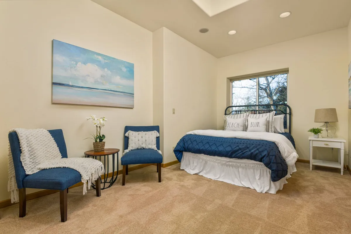 A spacious bedroom featuring a king-size bed with stylish bedding, artwork on the wall, and a tranquil sitting area with comfortable seating by a sunlit window. The overall atmosphere is cozy and serene, ideal for relaxation and privacy.
